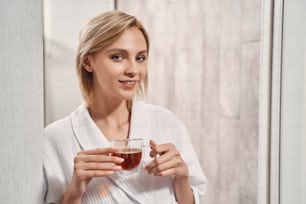 Portrait of a cute woman with a cup of black tea standing in the doorway