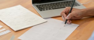 Close up view of male UI developer drawing on paperwork while looking information on laptop