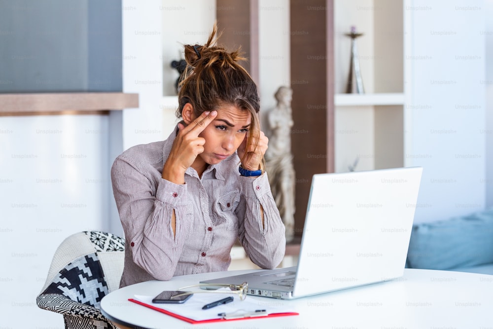 Jovem mulher frustrada que trabalha na mesa do escritório na frente do laptop que sofre de dores de cabeça diárias crônicas, tratamento on-line, nomeação para uma consulta médica, radiação eletromagnética, auxílio-doença