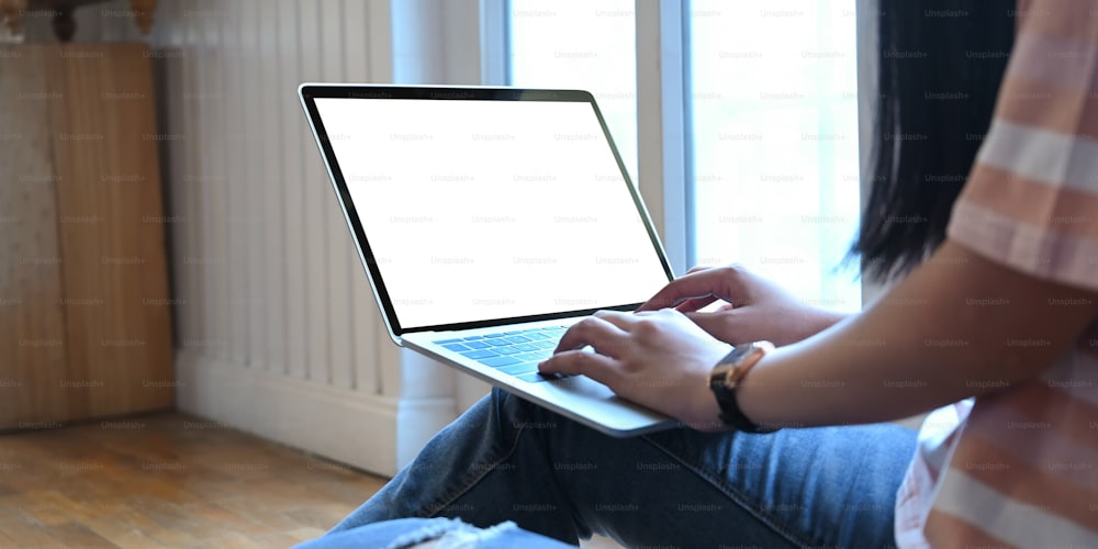 L'immagine ritagliata di una donna sta digitando su un computer portatile con schermo bianco e vuoto che mette in grembo.