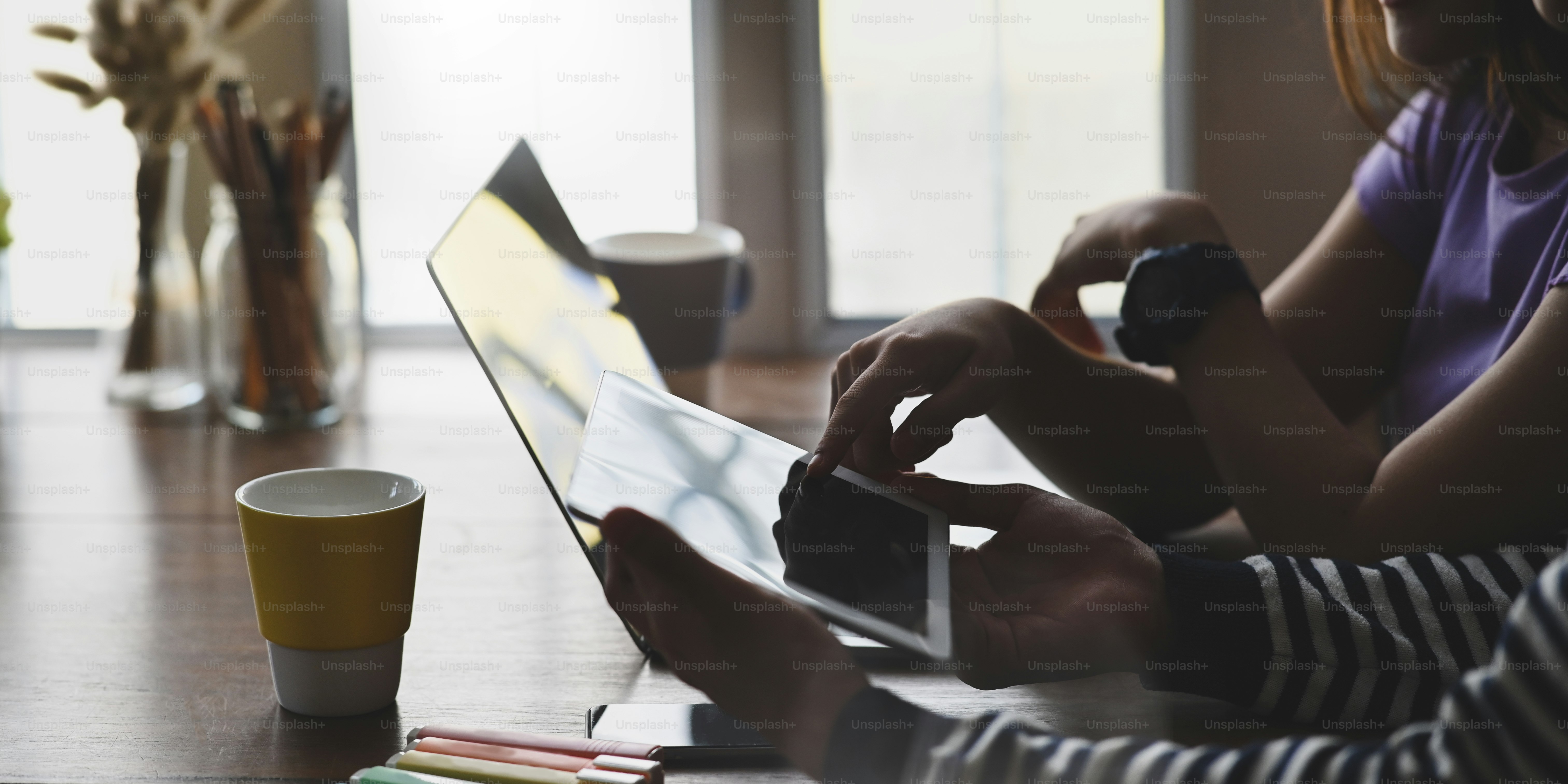 A young couple is working together with a computer laptop and tablet at the wooden working desk.
