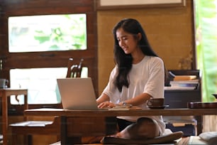 Una bella donna sta digitando su un computer portatile al tavolo di legno a gambe corte.