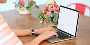 A beautiful woman is typing on a white blank screen computer laptop at the wooden working desk.