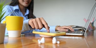 Cropped image of an office woman is charging a smartphone with a wireless charger while typing on a computer laptop.