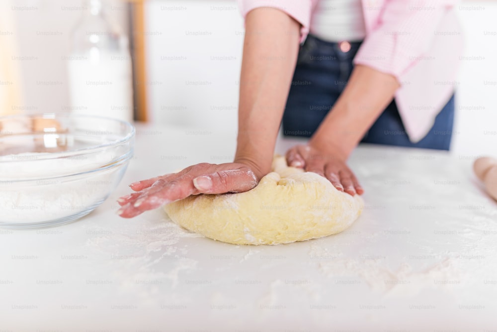 Close up of female baker hands kneading dough and making bread. cooking and home concept - close up of female hands kneading dough at home