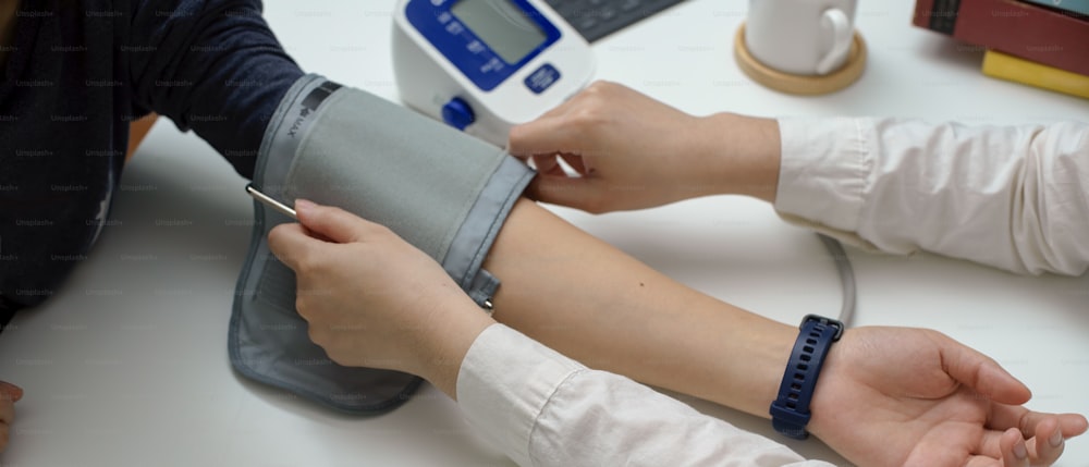 Plan recadré d’un médecin mesurant la pression de son patient avec un tensiomètre dans la salle d’examen