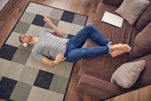 Hübscher brünetter Mann liegt auf farbigem Teppich und entspannt sich, während er Musik über Kopfhörer hört