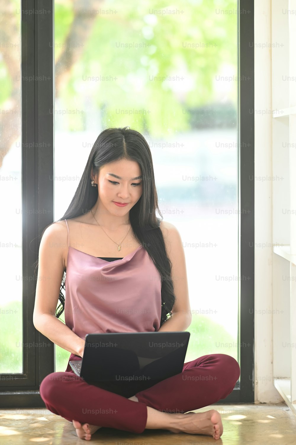 Asian woman using her laptop and sitting on floor in living room.