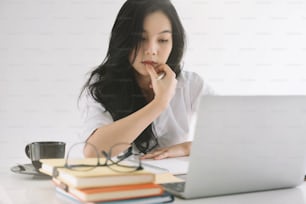 Young attractive woman using laptop while taking note on notepad at office.