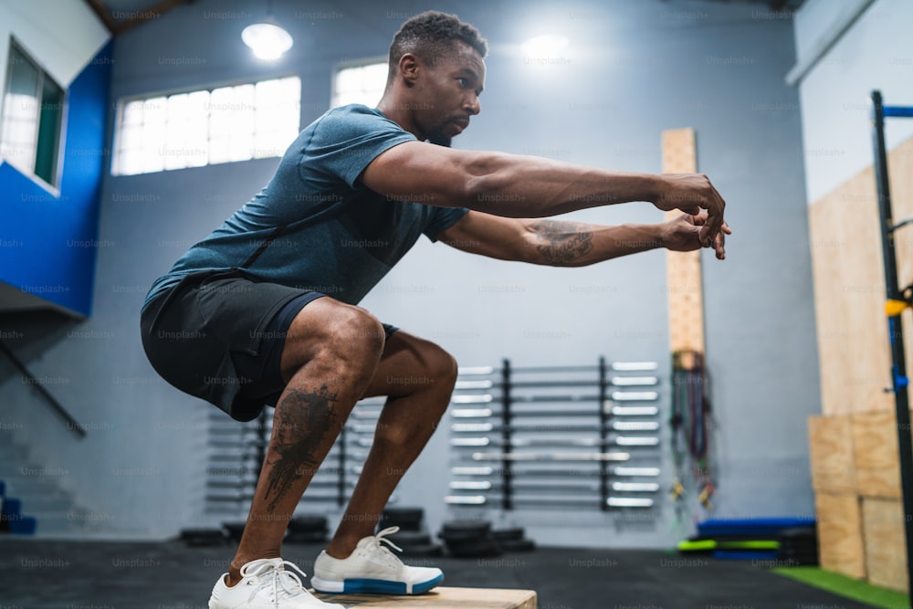 Ritratto di un uomo atletico che fa esercizio di salto in scatola. concetto di palestra, sport e stile di vita sano.