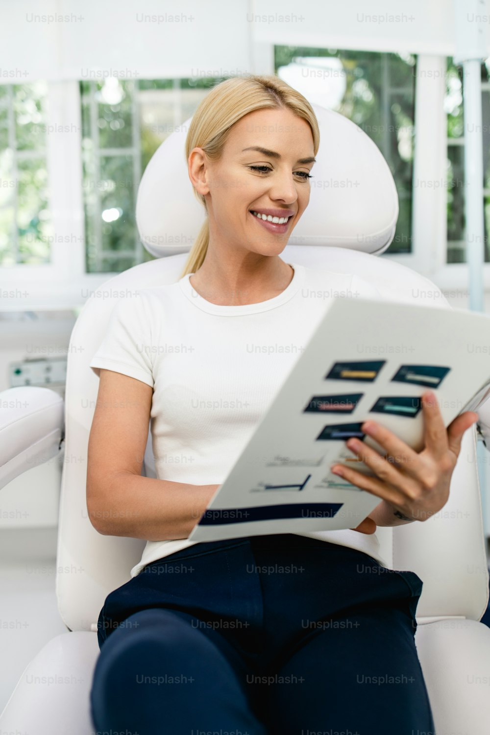 Beautiful and happy blonde woman at beauty medical clinic. She is sitting and reading clinic info about face and body beauty treatments.