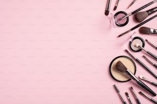 Composición plana con brochas de maquillaje y cosméticos faciales aislados sobre fondo rosa. Vista superior con espacio de copia. Maqueta de banner de salón de belleza. Set de maquillaje cosmético de moda
