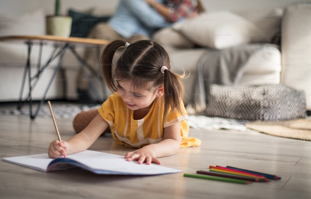 Homework. Family at home. Little girl writing on floor. Focus in on foreground.