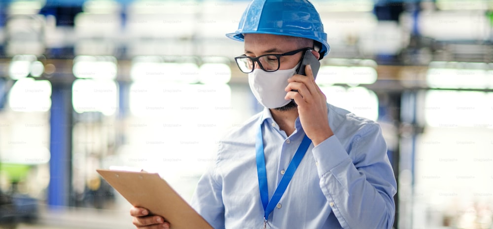 Man technician or engineer with protective mask and telephone working in industrial factory.