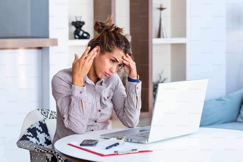 Jovem mulher frustrada que trabalha na mesa do escritório na frente do laptop que sofre de dores de cabeça diárias crônicas, tratamento on-line, nomeação para uma consulta médica, radiação eletromagnética, auxílio-doença