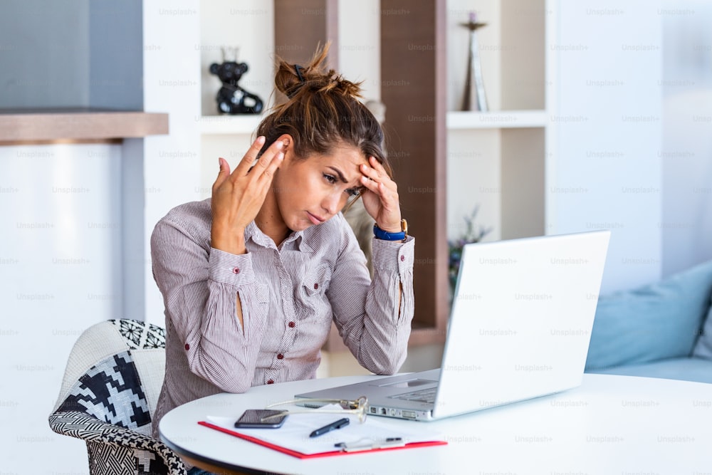 Young frustrated woman working at office desk in front of laptop suffering from chronic daily headaches, treatment online, appointing to a medical consultation, electromagnetic radiation, sick pay