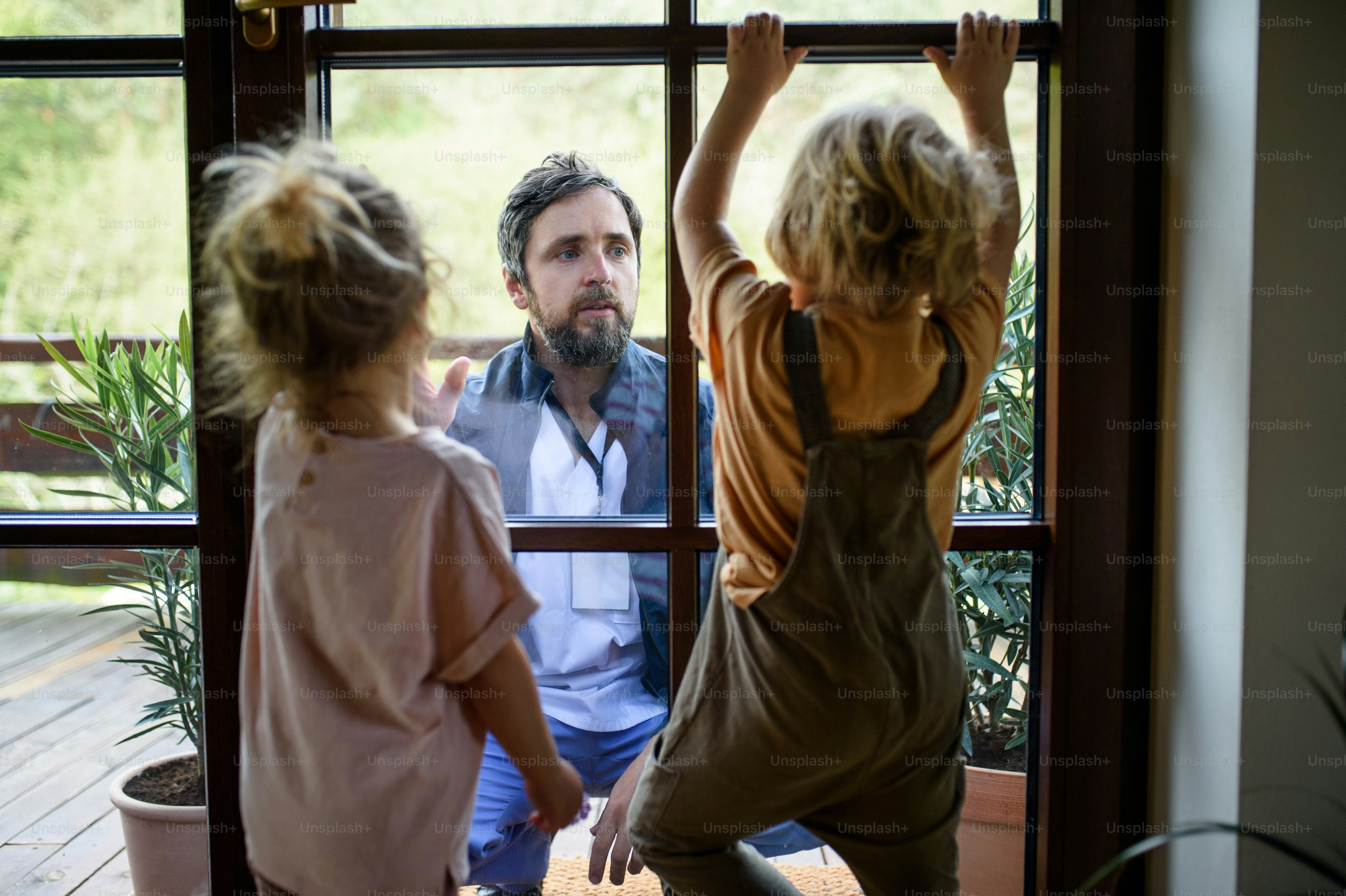 Doctor coming to see and greet family in isolation, window glass separating them.