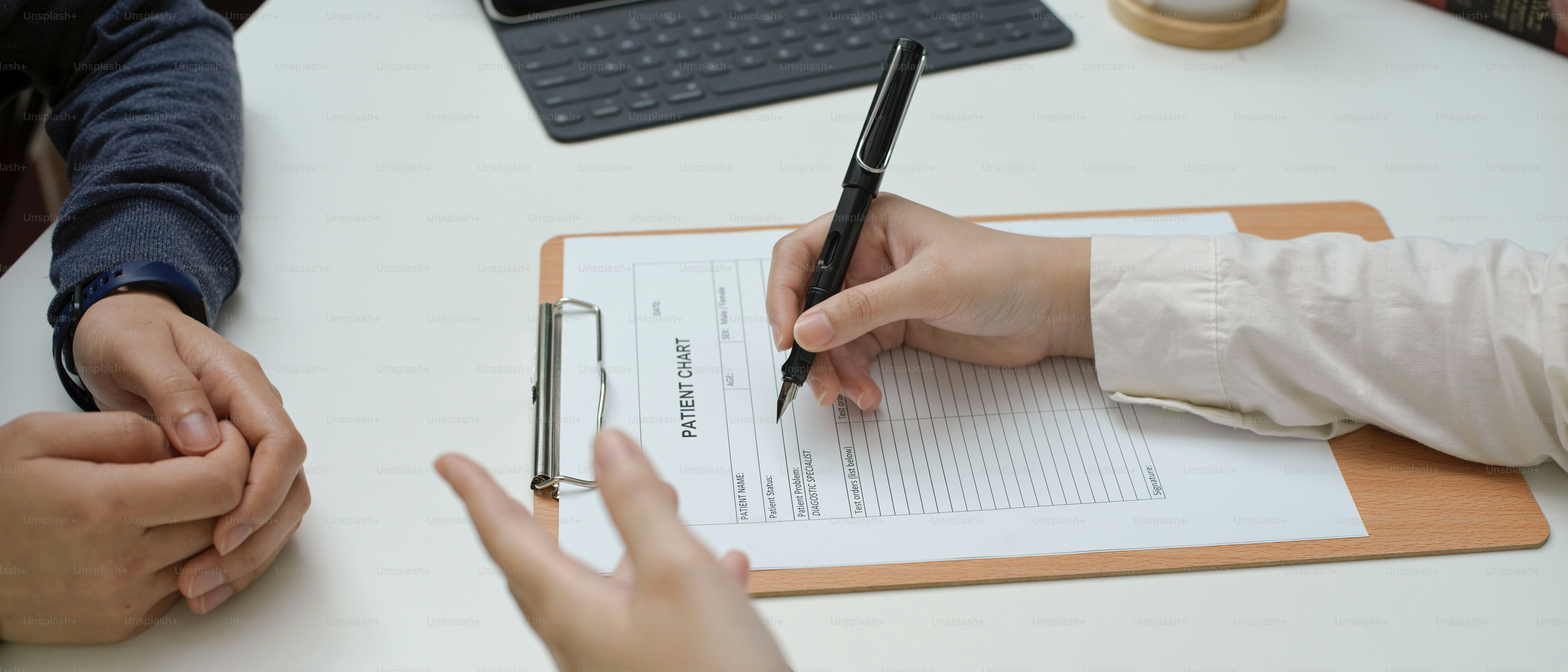 Side view of female doctor medical history taking and writing on patient chart in examination room