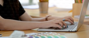 Vista lateral do designer feminino digitando no laptop com outros suprimentos do designer na mesa de trabalho de madeira