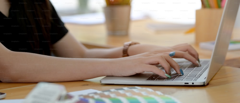 Side view of female designer typing on laptop with other designer supplies on wooden worktable