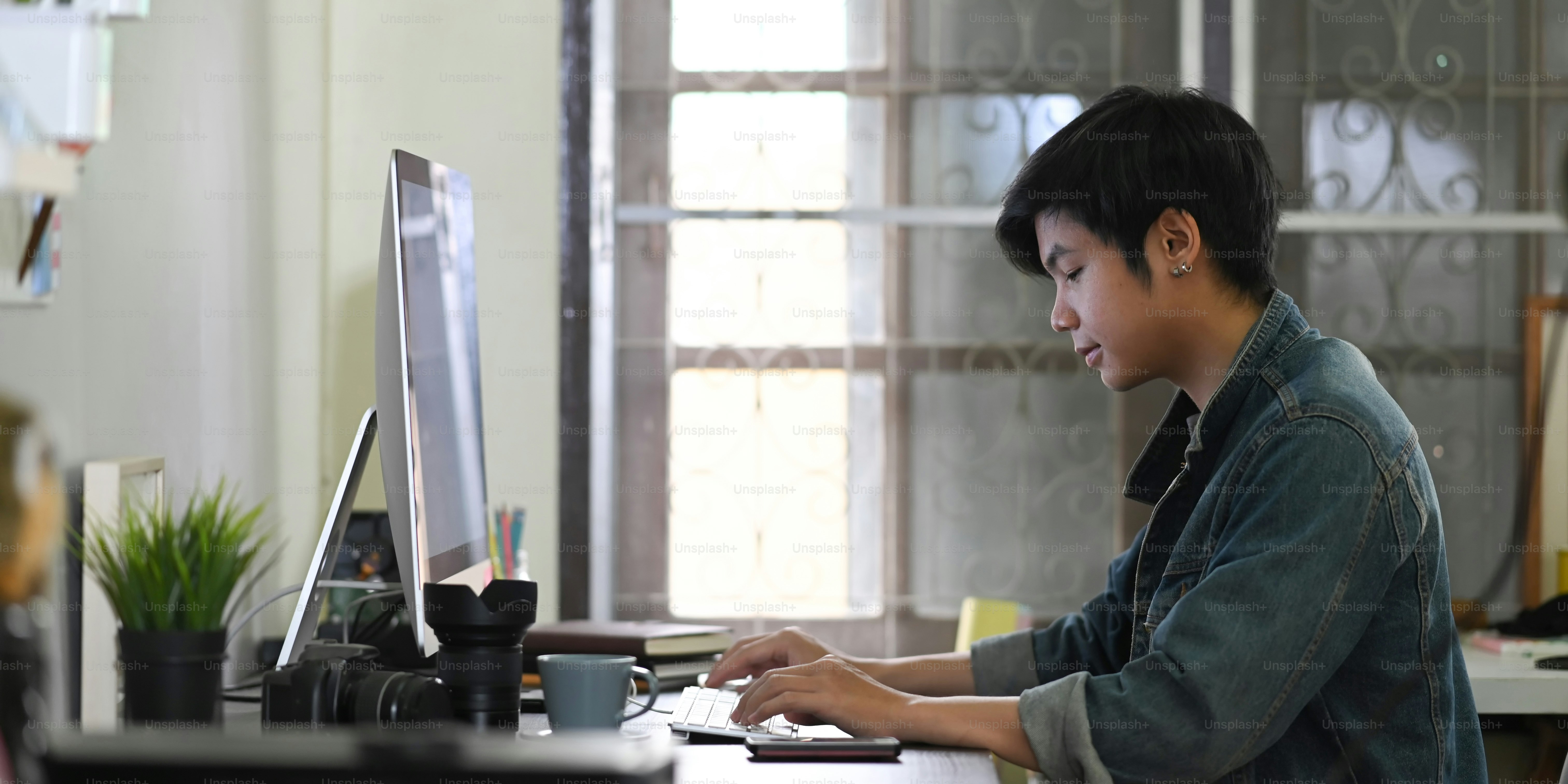 Ein kluger Mann tippt auf einer Tastatur am Schreibtisch, umgeben von Fotografenausrüstung.