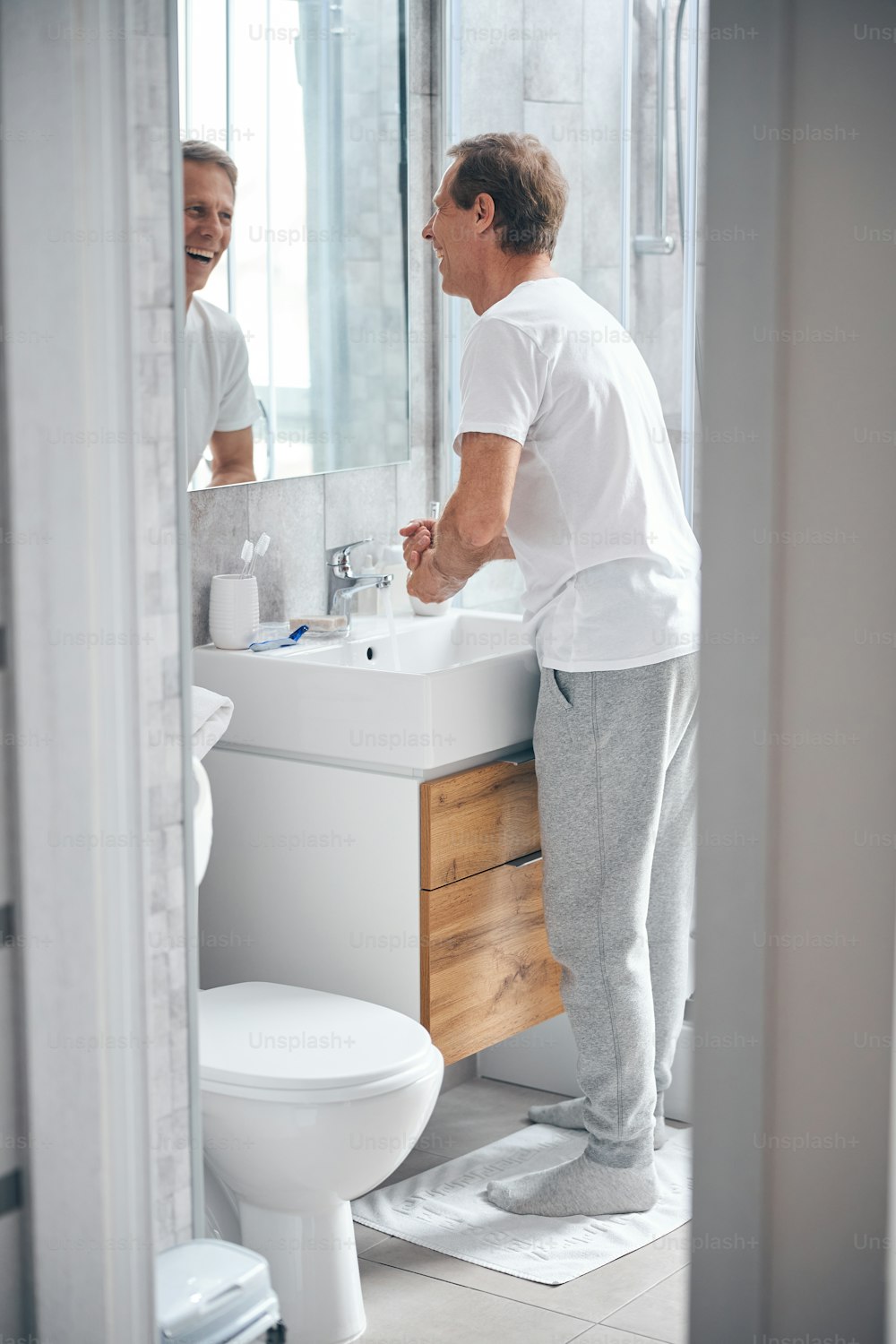 Vista lateral de um homem olhando para si mesmo no espelho durante o procedimento de lavagem das mãos