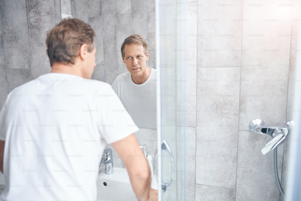 Retrato de un hombre adulto caucásico serio que mira fijamente su reflejo en el espejo