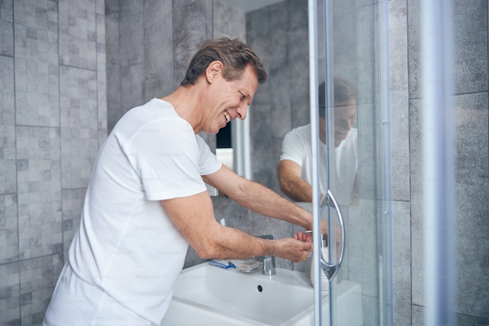 Side view of a joyful Caucasian male squeezing the liquid soap out of the dispenser