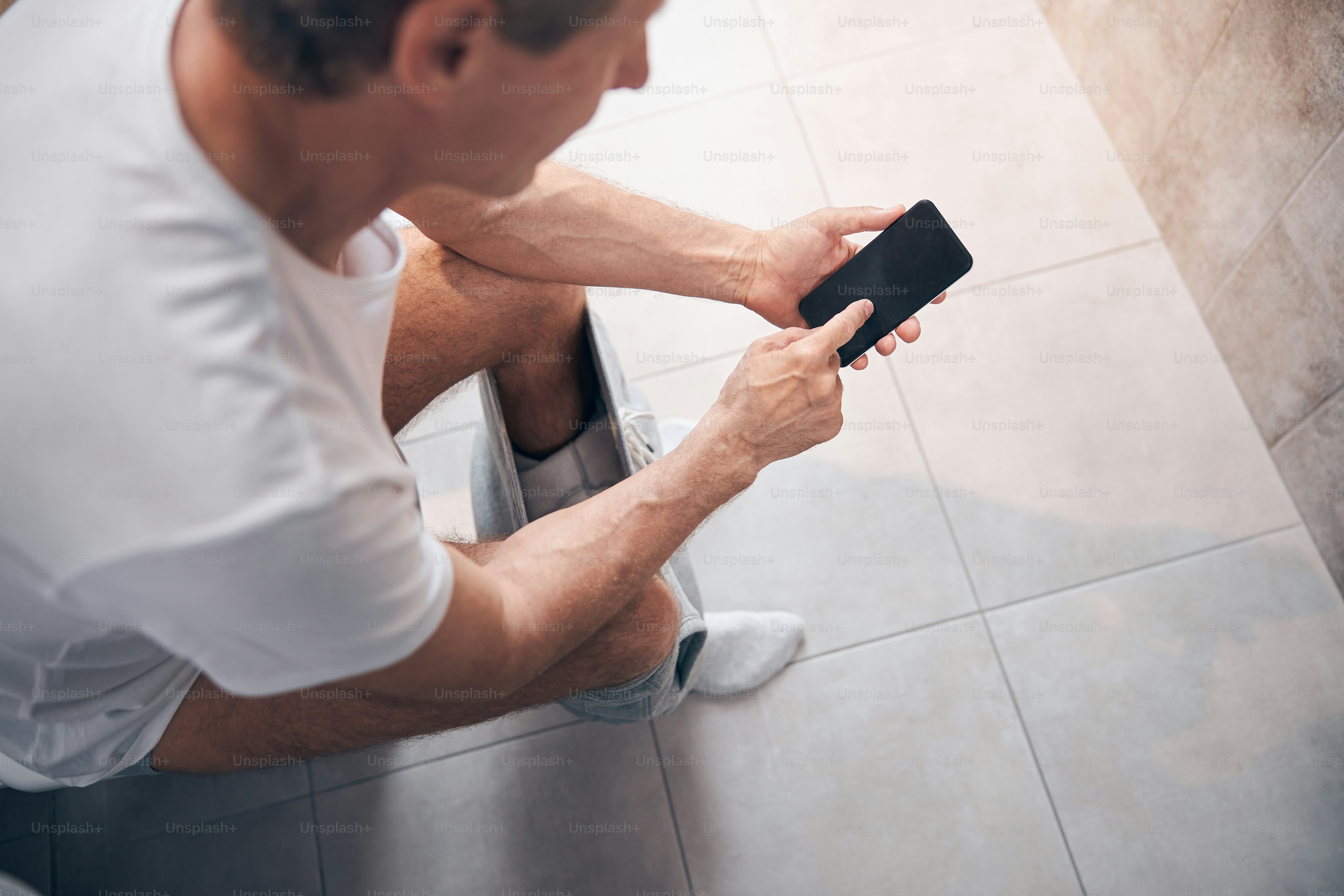 Top view of a short-haired adult man in a cotton t-shirt using his mobile phone