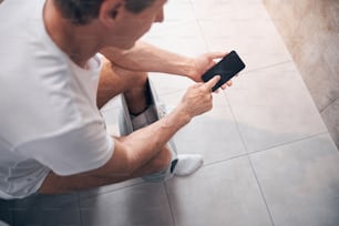 Vista dall'alto di un uomo adulto dai capelli corti in una maglietta di cotone che usa il suo telefono cellulare