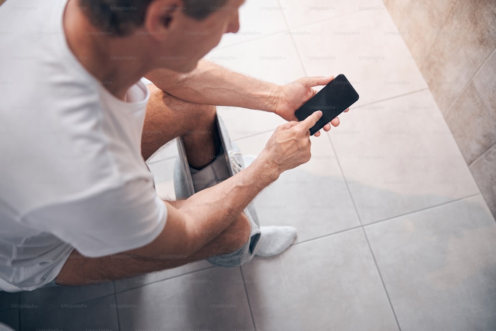 Top view of a short-haired adult man in a cotton t-shirt using his mobile phone