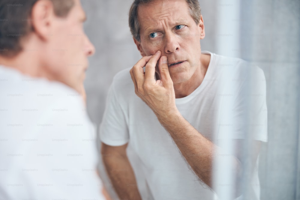Close up portrait of a male doing a skin checkup before the mirror on the wall