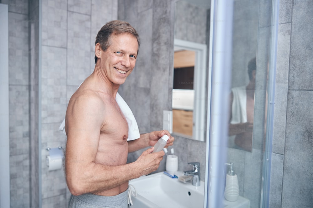 Waist-up portrait of a handsome short-haired male with an aftershave cologne smiling at the camera