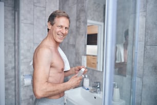 Taillenporträt eines gutaussehenden kurzhaarigen Mannes mit einem Aftershave-Kölnischwasser, das in die Kamera lächelt