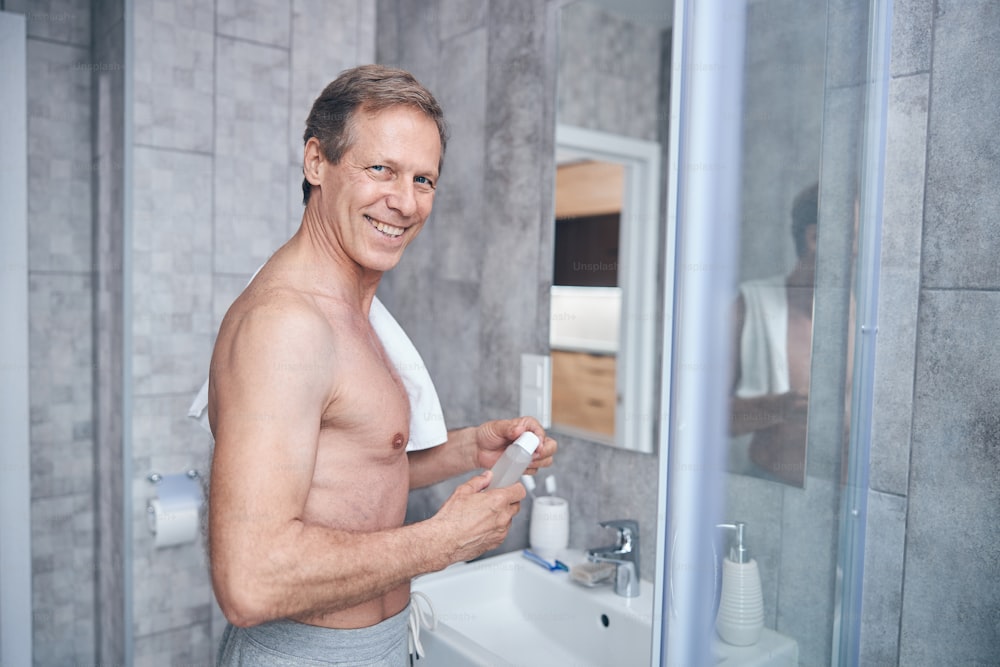Taillenporträt eines gutaussehenden kurzhaarigen Mannes mit einem Aftershave-Kölnischwasser, das in die Kamera lächelt