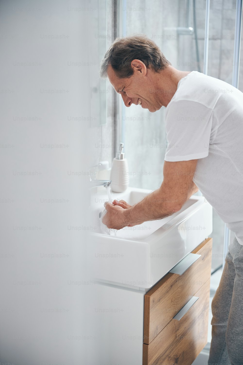 Side view of a smiling male cleaning his hands with warm water in the bathroom