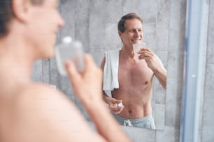 Porträt eines attraktiven übermütigen Mannes, der eine Flasche Aftershave-Lotion an seine Nase hält