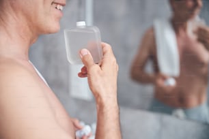Cropped photo of a smiling man inhaling the aroma of toilet water in his hand