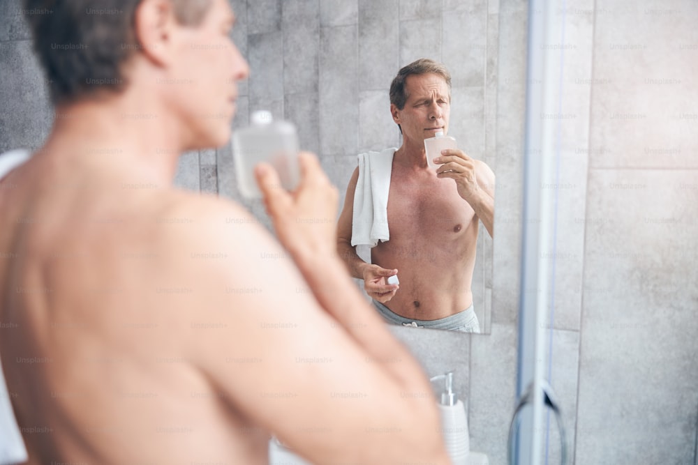 Porträt eines gelassenen Mannes mit geschlossenen Augen, der sein Toilettenwasser im Badezimmer riecht