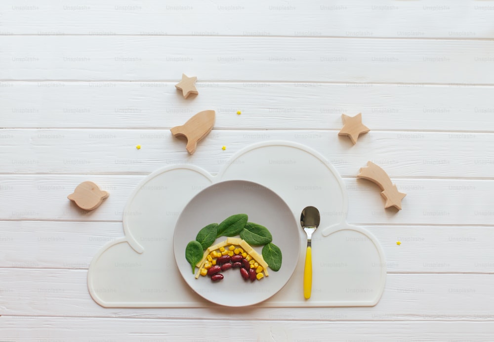 Healthy food for children concept. Rainbow from beans, corn, cheese and spinach on white wooden background with blank space for text. Top view, flat lay.