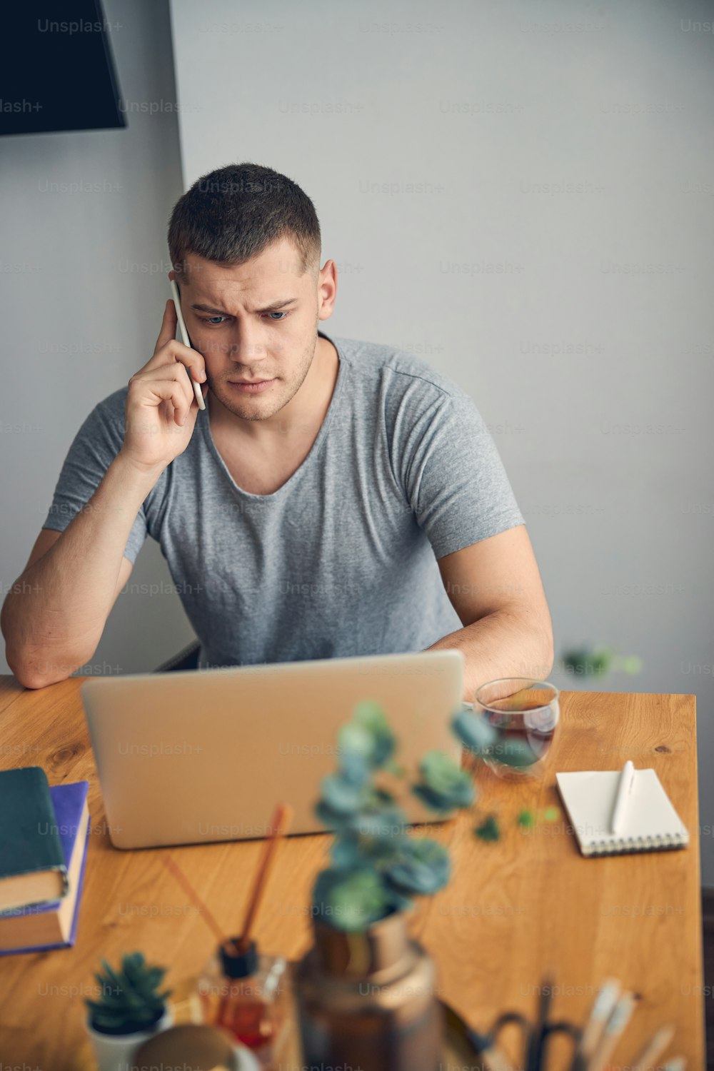 Serious brunette man in grey T-shirt working online from home and calling someone to speak