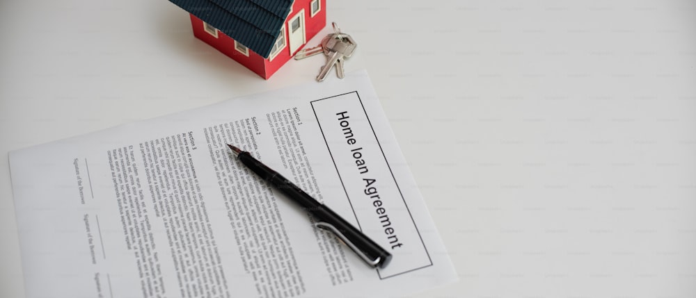 白いテーブルの上にペン、家のモデル、家の鍵を持つ住宅ローン契約の上面図