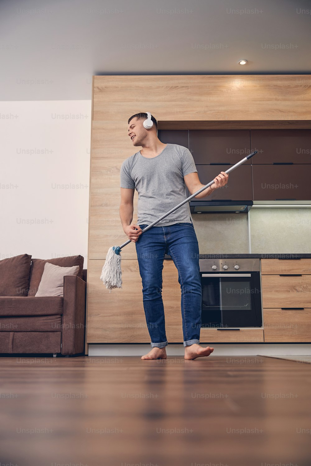 Handsome brunette male in casual clothes with headphones washing floor with mopping stick