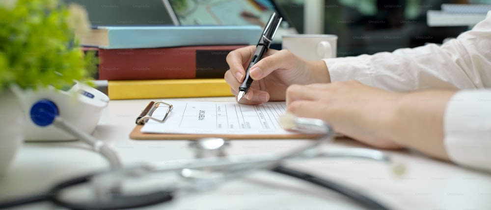 Vue latérale d’un médecin rédigeant une ordonnance alors qu’il est assis à une table de travail dans la salle d’examen