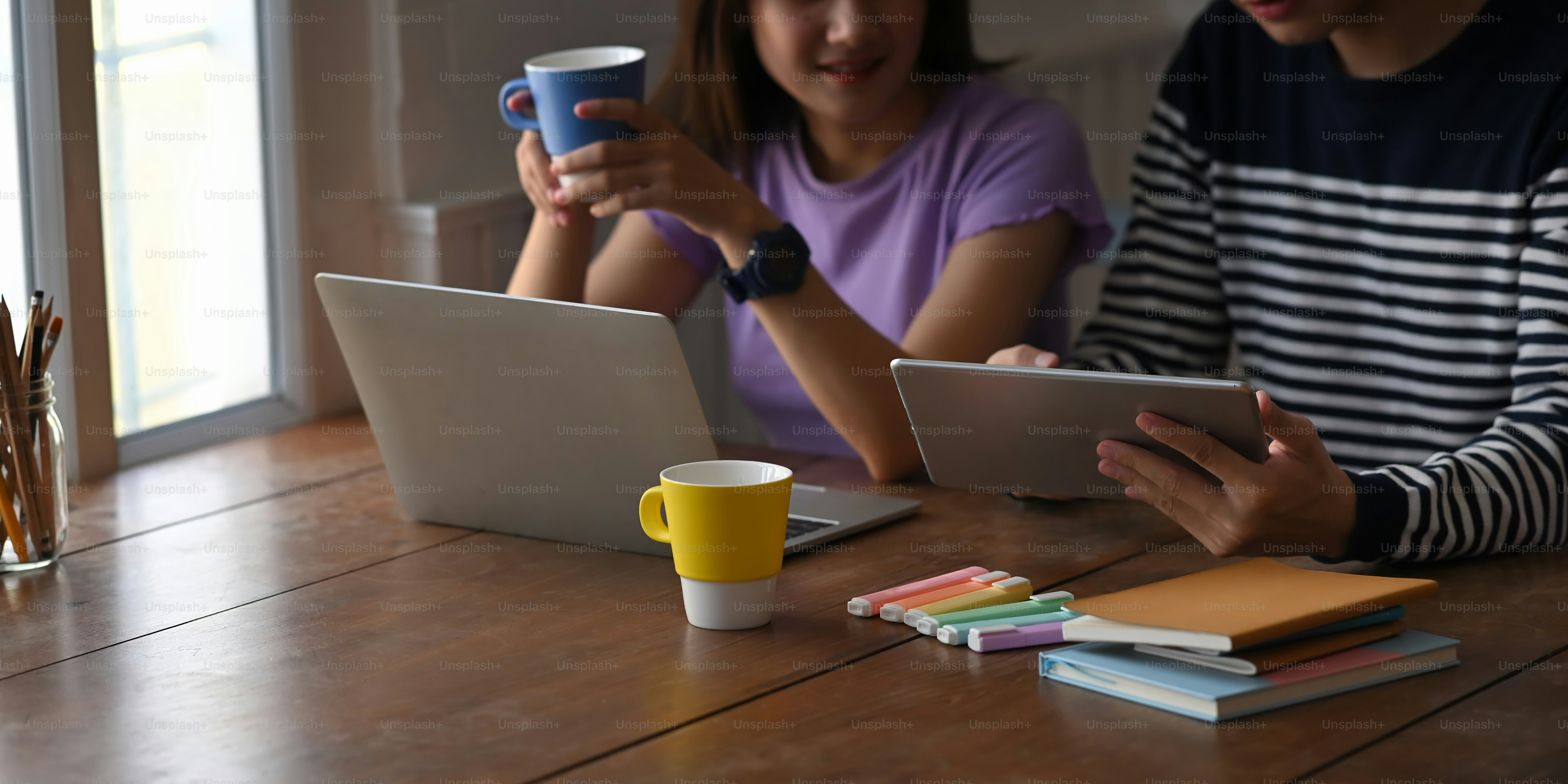A young couple is working together with a computer laptop and tablet at the wooden working desk.