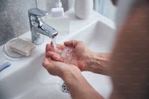 Cropped photo of a Caucasian male holding his cupped palms under the faucet with running water