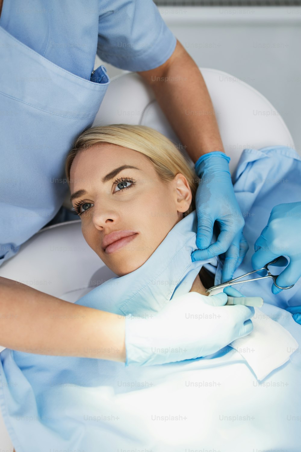 Beautiful young blonde woman receiving mole or birthmark removal treatment at beauty clinic. Medical surgery for body and face corrections concept. View from above.