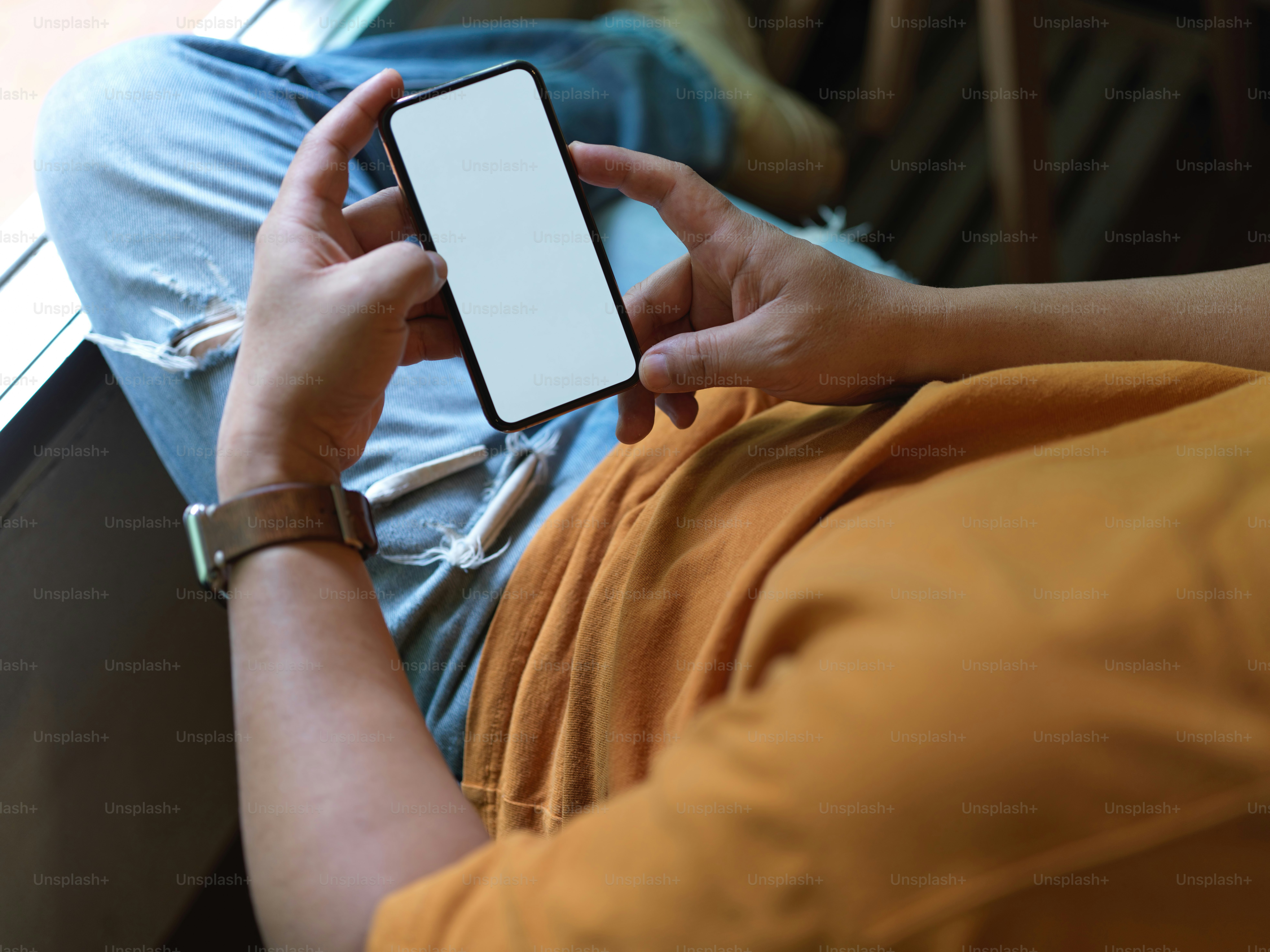 Close up view of male freelancer resting with mock-up smartphone while lying relaxed on office chair near window