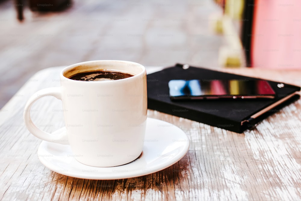 taza de café y teléfono inteligente al aire libre en una mesa en una cafetería o cafetería con fondo borroso