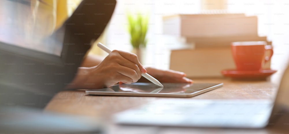 Businesswomen are working together by using a computer laptop and tablet at the wooden working desk.